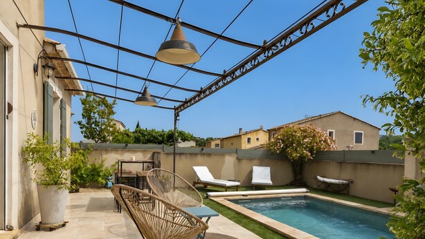 A poolside area with lounge chairs, a table, and a potted plant. - Charming Villa in St Rémy de Provence with Pool (Saint-Rémy-de-Provence)