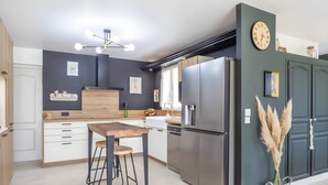 A modern kitchen with a wooden table, bar stools, a stainless steel refrigerator, and a clock on the wall. - Charming Villa in St Rémy de Provence with Pool (Saint-Rémy-de-Provence)