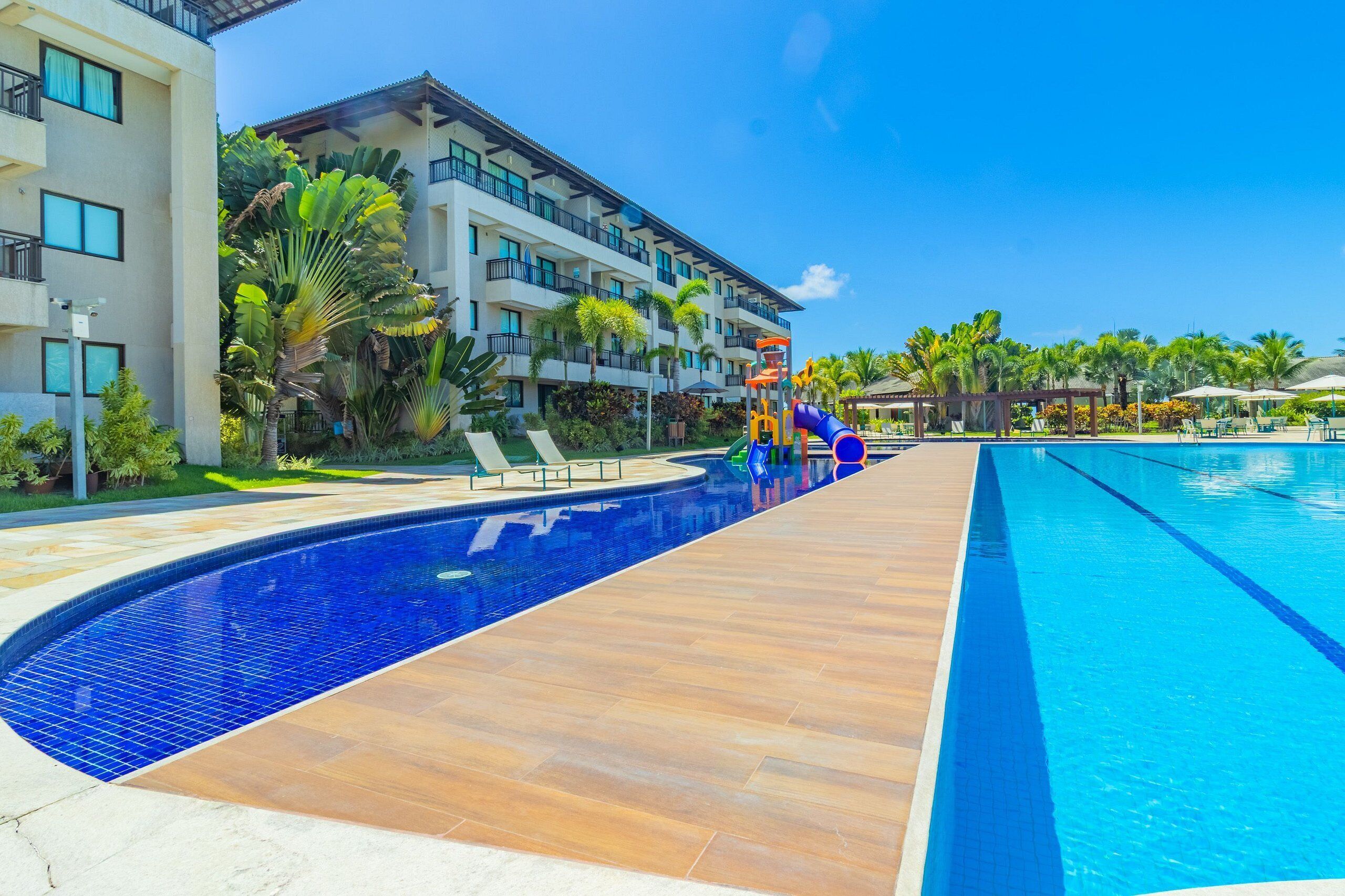 A resort pool with a slide, palm trees, and a multi-story building with balconies.