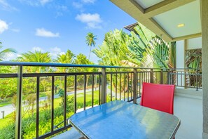 A balcony with a metal table and red chair, overlooking a well-maintained garden with palm trees and a road. - Eco Life #105 - Apt With Balcony by Carpediem (Ipojuca)