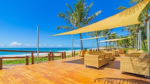 Um deck de madeira com móveis de vime e vista para o oceano.
