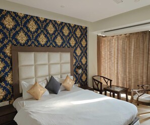 Une chambre d’hôtel avec un grand lit, une tête de lit, une petite table, deux chaises et une fenêtre avec des rideaux.