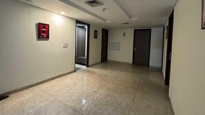 Un couloir avec une alarme incendie, une porte et un sol carrelé.