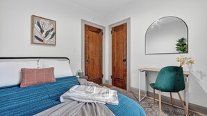 A bedroom with a bed, a desk, and a chair. There is a mirror on the wall above the desk.