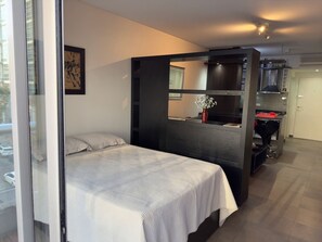 A bedroom with a large bed, a dark partition, and a kitchenette area. - Palermo Hollywood: Manhattan views and fine dining (Buenos Aires)