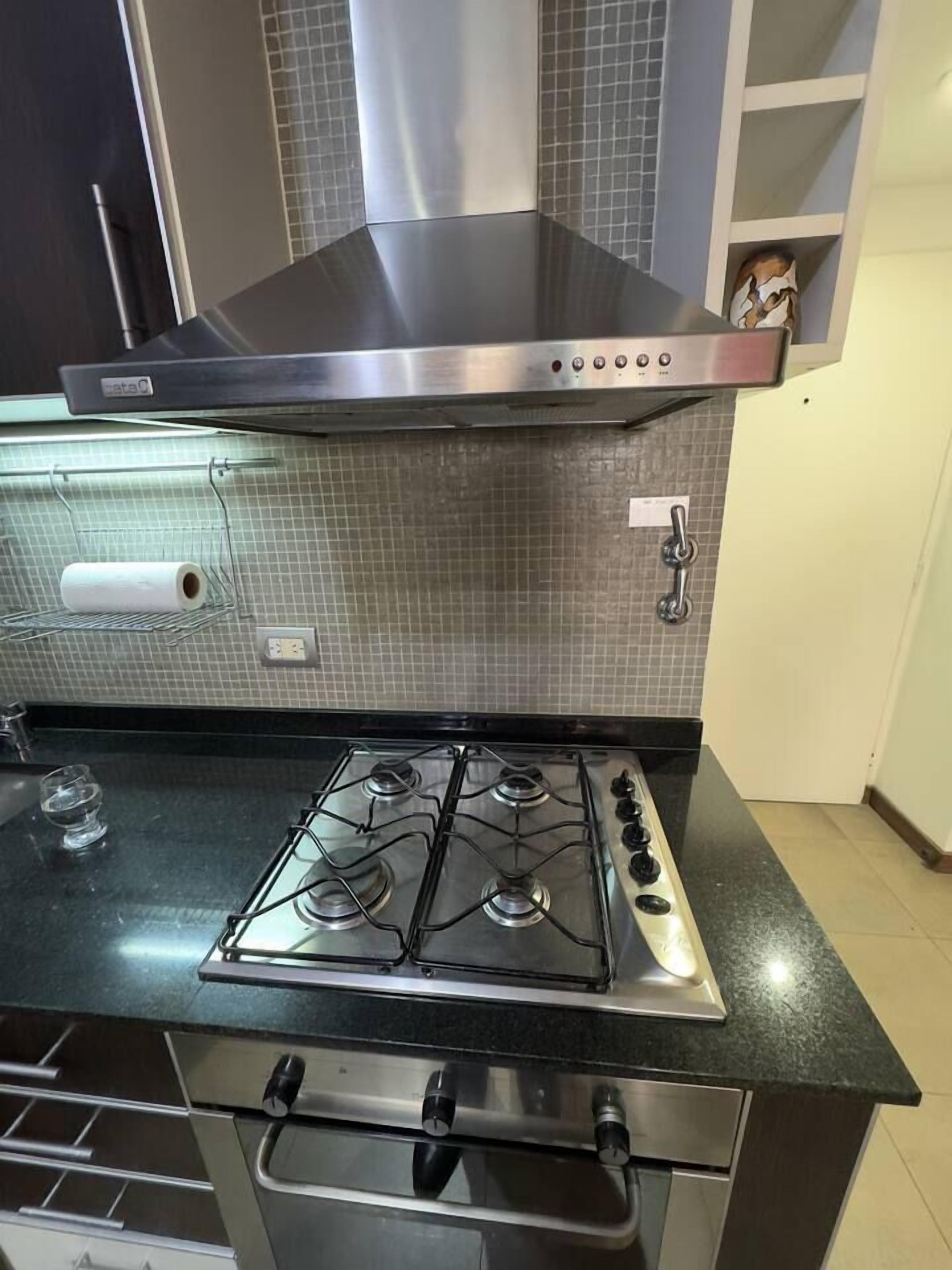 A kitchen with a stainless steel stove, a black range hood, and a tiled backsplash.