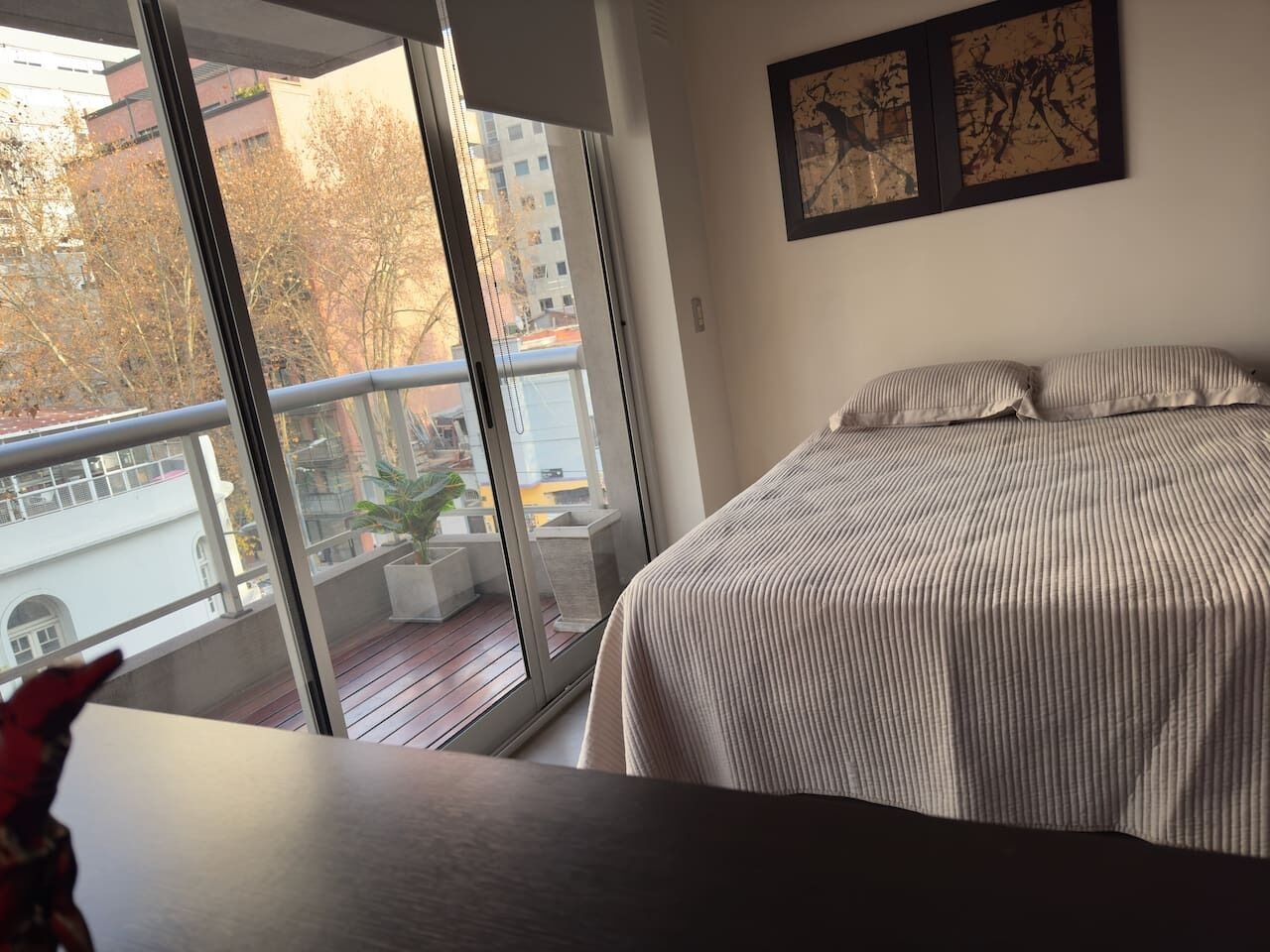 Quarto com uma grande janela, uma cama com roupa de cama listrada e duas obras de arte emolduradas na parede.