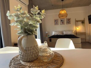 Quarto de hotel com cama, mesa de cabeceira e um vaso decorativo com flores sobre um jogo americano trançado.