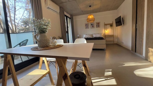 Una sala de estar moderna con un sofá blanco, una mesa de comedor con un jarrón y un ventanal con cortinas.