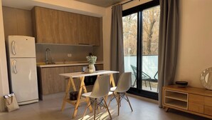 Una cocina moderna con armarios de madera, un refrigerador blanco, una mesa de comedor con dos sillas y vistas a los árboles por la ventana.