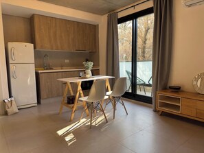 Een moderne keuken met houten kastjes, een witte koelkast, een eettafel met twee stoelen en uitzicht op bomen door het raam.