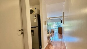 Un pasillo con suelo de madera, una puerta blanca y una zona de cocina con refrigerador y microondas.