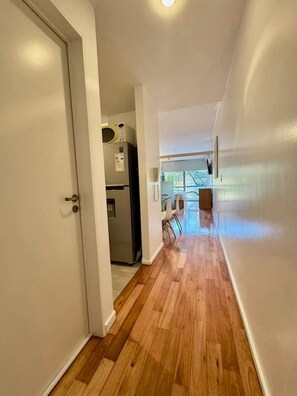 Ein Korridor mit Holzboden, einer weißen Tür und einem Küchenbereich mit Kühlschrank und Mikrowelle.