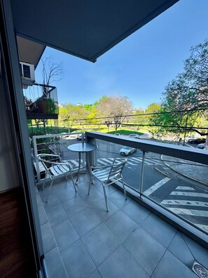Ein Balkon mit Blick auf einen Park, einem Tisch und Stühlen.