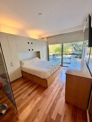 Een moderne slaapkamer met een bed, een inbouwkast en een balkon met tuinmeubilair.