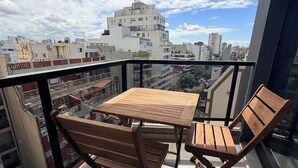 A balcony with a wooden table and chairs, a glass railing, and a city view. - Palermo Portẽnito: A Cosmopolitan Nomad Oasis (Buenos Aires)