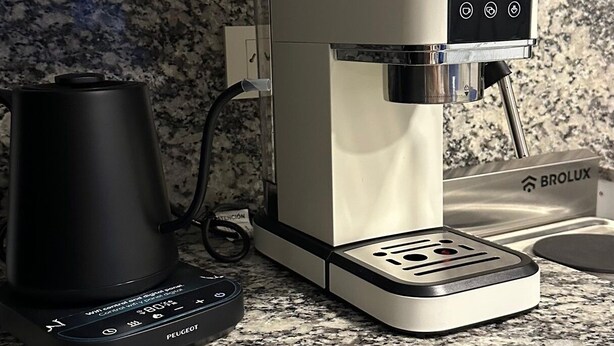 Una màquina de cafè amb un panell de control i una tetera sobre una superfície de granit.