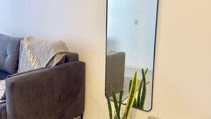 Un soggiorno moderno con un divano grigio, un grande specchio, una pianta in vaso e un cuscino decorato.
