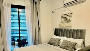 Una camera da letto con un letto grande, una decorazione a macramè appesa al muro e un condizionatore d'aria fissato alla parete.