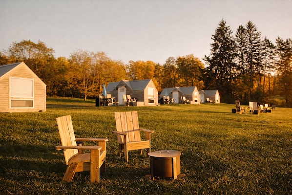 A grassy area with wooden chairs and a pot, a small shed, and several wooden cabins in the background.