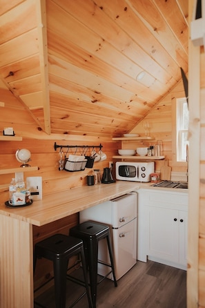 A compact kitchen with wooden walls, a microwave, a toaster, and a small refrigerator.