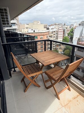 Un balcon avec une table et des chaises en bois, donnant sur un paysage urbain.