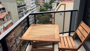 Ein Balkon mit Holztisch und zwei Stühlen, mit Blick auf eine Stadtlandschaft mit verschiedenen Gebäuden.