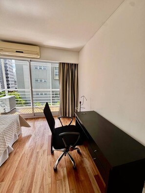 A modern hotel room with a wooden floor, a black office chair, a desk, and a bed with a white bedspread. - Big Palermo 5th floor suite with pool and Sauna (Buenos Aires)