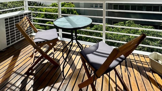 Un balcón con mesa y sillas, vista a edificios de la ciudad y cielo despejado.