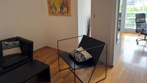 Ein modernes Wohnzimmer mit einer schwarzen Couch, einem schwarzen Metallstuhl und einem großen abstrakten Gemälde an der Wand.