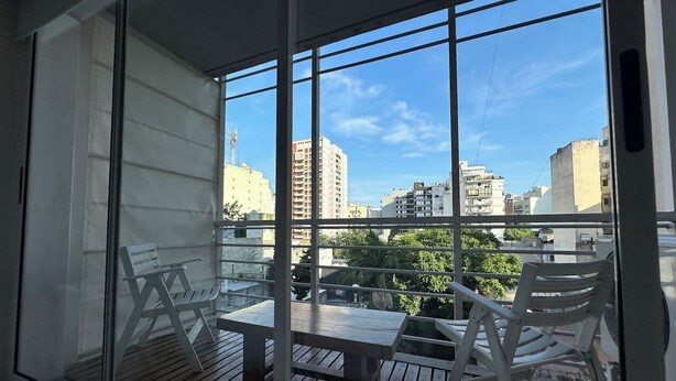 Ein Balkon mit Tisch und Stühlen, Blick auf die Stadt und ein klarer Himmel.