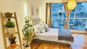 Ein modernes Schlafzimmer mit Holzboden, einem Bett mit gestreifter Bettwäsche, einem Himmelsbettregal mit Blumentöpfen und Blick auf Gebäude durch große Fenster.