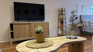 Ein Wohnzimmer mit einem Holz-TV-Schrank, einem großen Flachbildfernseher, einem gewölbten Couchtisch mit einer gewebten Unterlage und einem Sofa mit gestreiften Kissen.