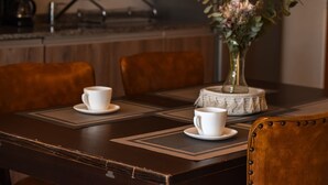 Un tavolo da pranzo con due tazze e piattini bianchi, un vaso con fiori e una macchina da caffè sullo sfondo.