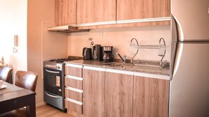 Una cucina compatta con mobili in legno, un fornello a gas, una macchina per il caffè e un frigorifero in acciaio inossidabile.