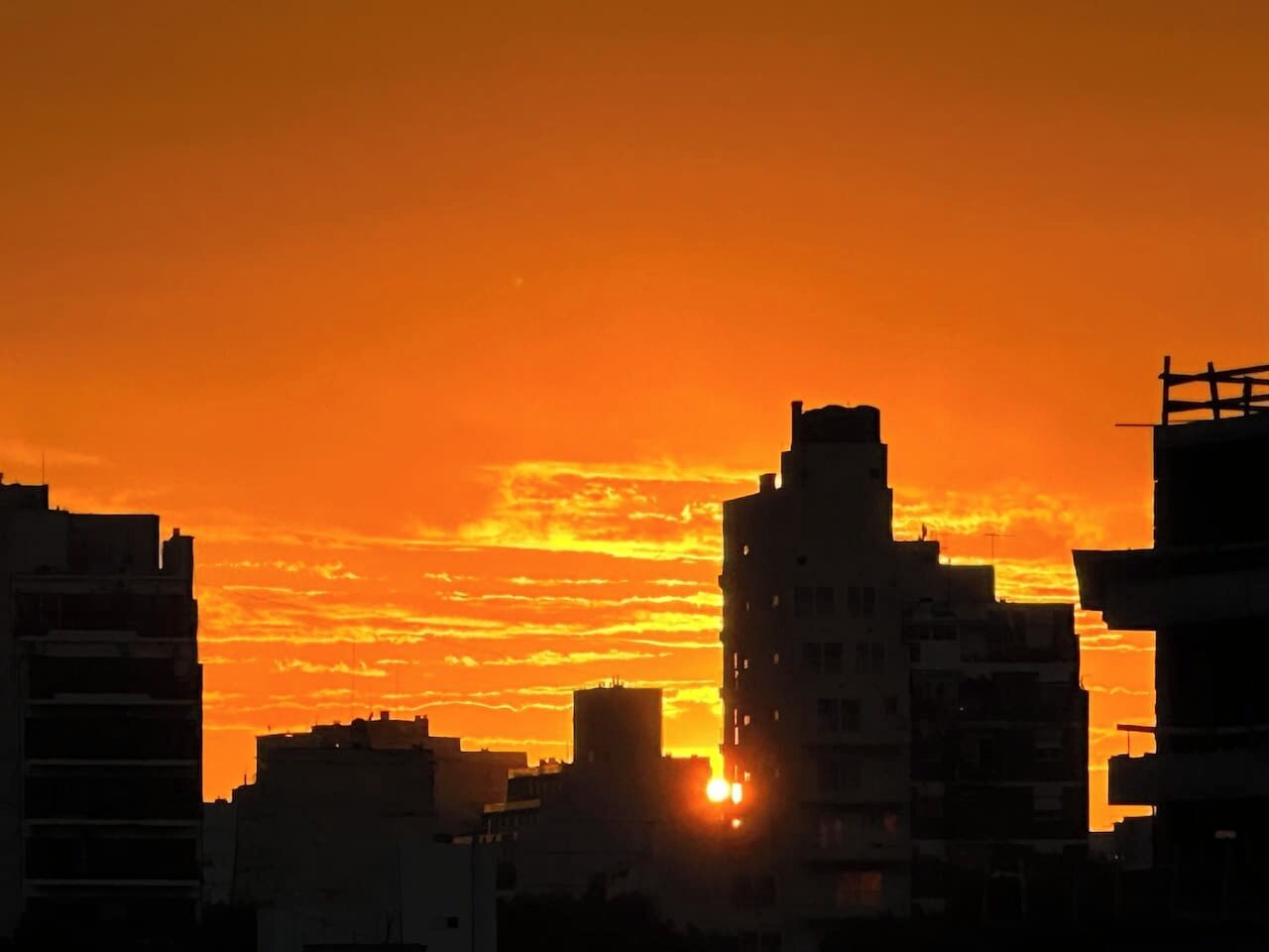 A cityscape at sunset with silhouettes of buildings against a vibrant orange sky.