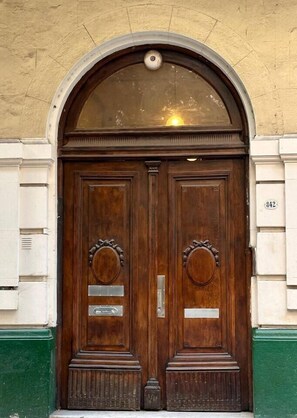 Uma porta dupla de madeira com arco semicircular acima, em um edifício com detalhes em branco e verde.