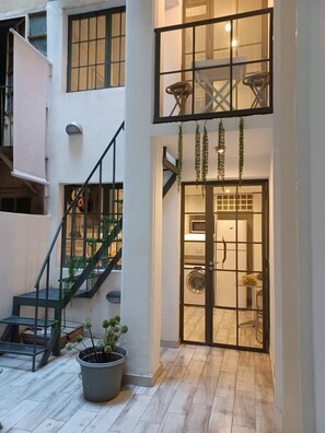 Apartamento com vários níveis, escada, planta em vaso e vista do interior por uma porta de vidro.