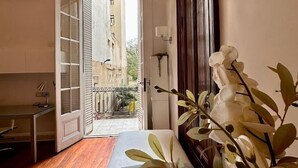 A room with a wooden floor, a white bench, a potted plant, and a view through an open door to a balcony with a railing. - Grand Rivadavia: 3-BR Ensuite High Ceiling Home (Buenos Aires)