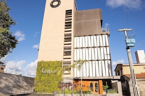 Ein modernes Gebäude mit einem hohen Uhrturm, einem Schild mit der Aufschrift "sense" und einer grünen Wand mit Pflanzen.