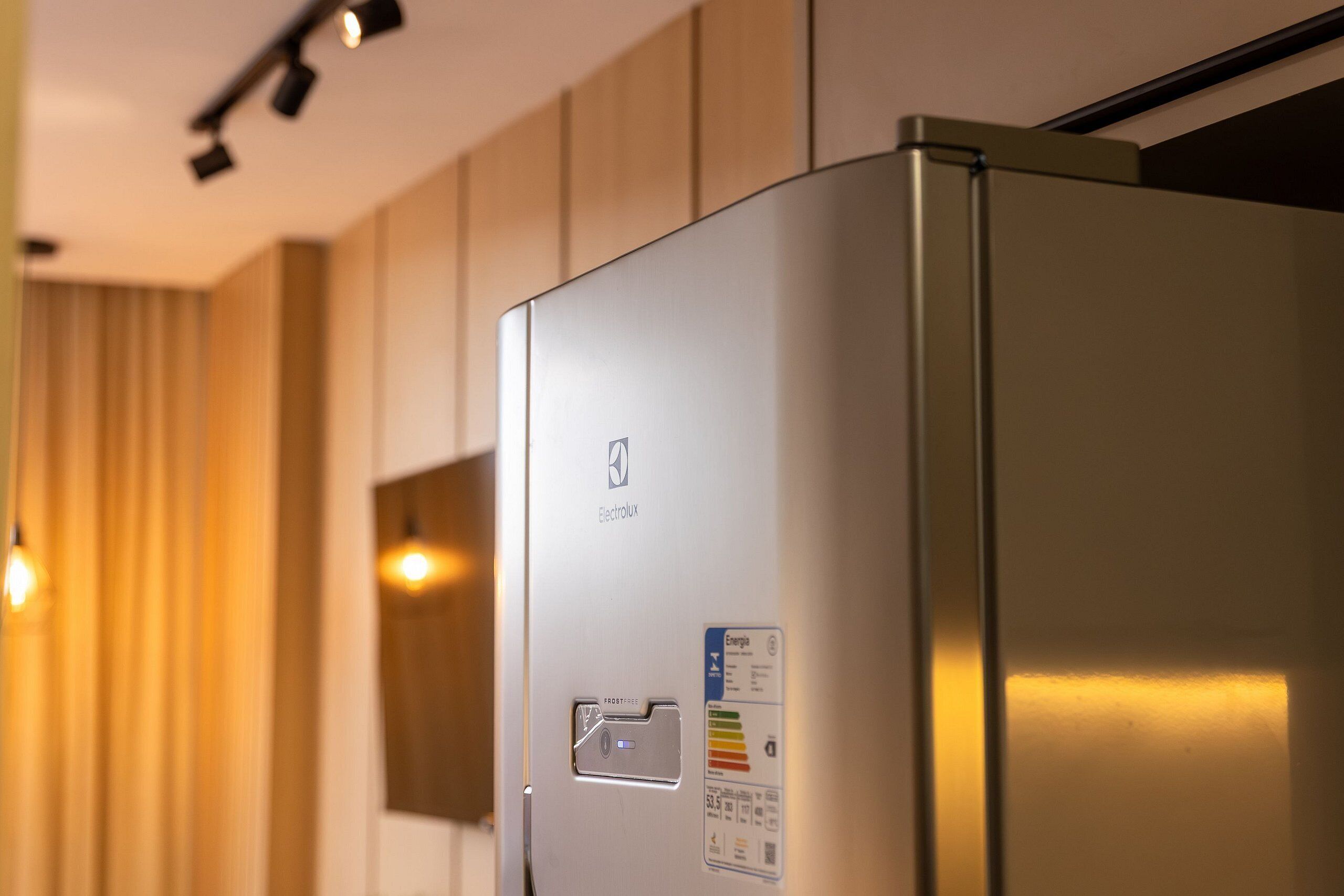 Eine moderne Küche mit Edelstahl-Kühlschrank, Holzschränken und Pendelleuchten.