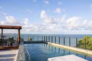 Ein Pool mit unendlicher Optik und Blick auf den Ozean, eine Holzterrasse und eine Pergola.