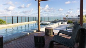 Een buitenzwembad met uitzicht op zee, een houten terras en ligbedden.