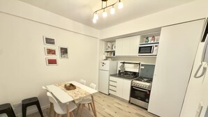Moderni keittiö, jossa on valkoiset kaapit, ruokapöytä tuoleineen ja mikroaaltouuni.