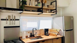 A compact kitchen with a stove, sink, and a built-in refrigerator. There are wooden cabinets and a window above the sink. - Plaza Serrano: Japandi -epicenter nest by airesB&B (Buenos Aires)