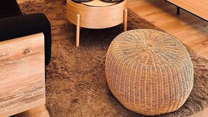 A modern living room with a wooden TV stand, a round coffee table, a woven pouf, and a large TV. - Plaza Serrano: Japandi -epicenter nest by airesB&B (Buenos Aires)