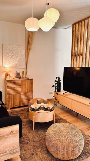 Ett modernt vardagsrum med ett TV-bord i trä, ett runt soffbord, en vävd pall och en stor TV.