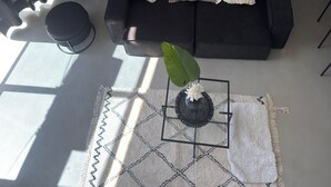 A modern living room with a black sofa, a hanging light fixture, a potted plant, and a patterned rug. - Plaza Serrano Front Row Loft by airesB&B (Buenos Aires)