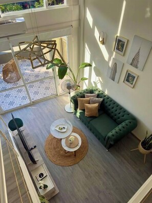 A spacious living area with a green sofa, two round tables, and a large window providing natural light. - Plaza Serrano: Casa Dorada luxury loft by airesB&B (Buenos Aires)