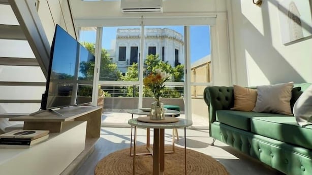 A spacious living room with a large window, a green sofa, a coffee table, and a TV on a stand. - Plaza Serrano: Casa Dorada luxury loft by airesB&B (Buenos Aires)